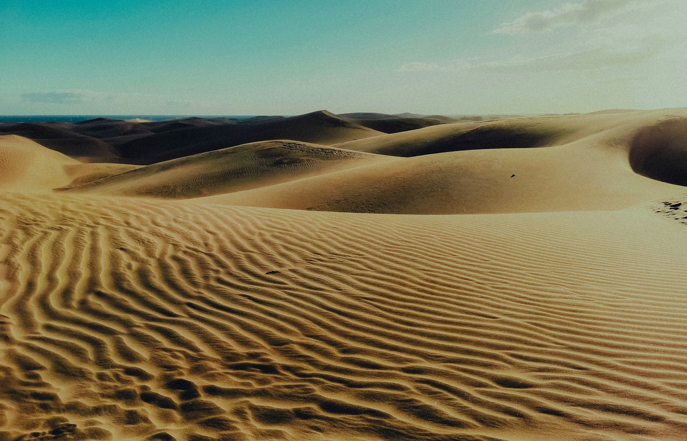 Rippled sand and rolling dunes at Maspalomas beneath a blue-green sky