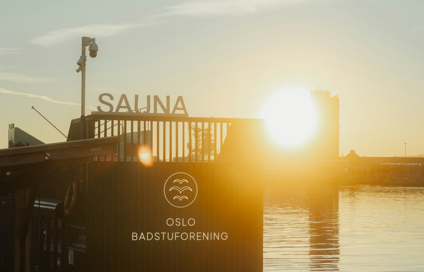 An Oslo Badstuforening waterfront sauna and its upper terrace backlit by the setting sun