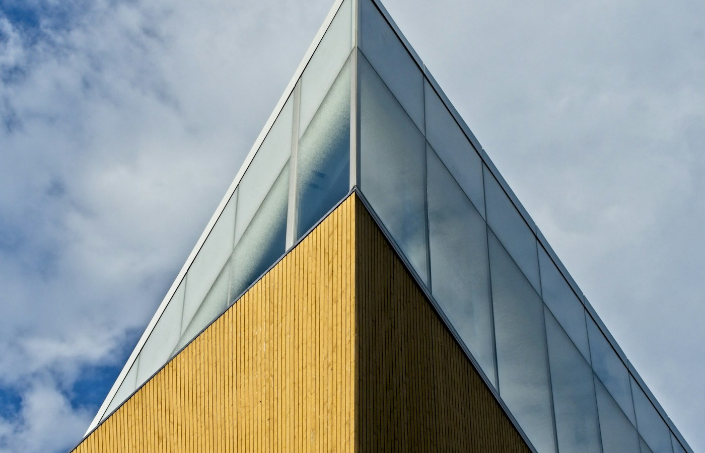 The angular timber-clad corner and dark glazed upper façade of Helsinki's Oodi library beneath a blue sky