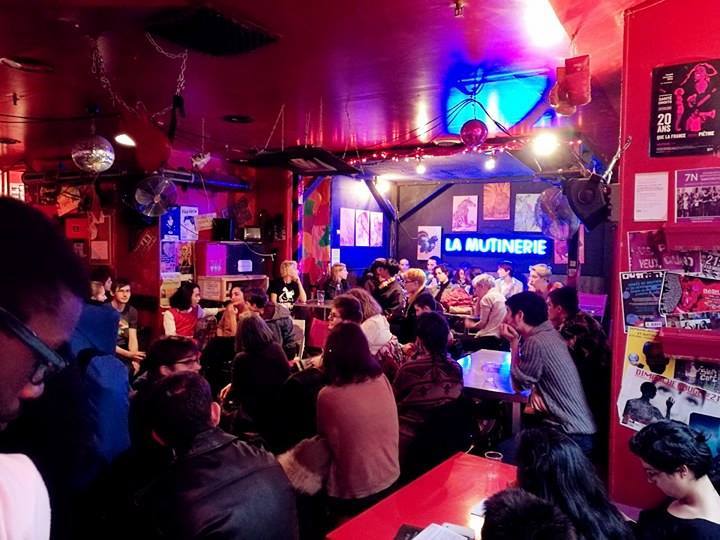 Guests inside La Mutinerie, with colourful lighting and the bar name on the wall
